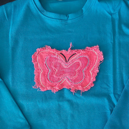 Blue shirt with a pink embroidered heart design on a plain background